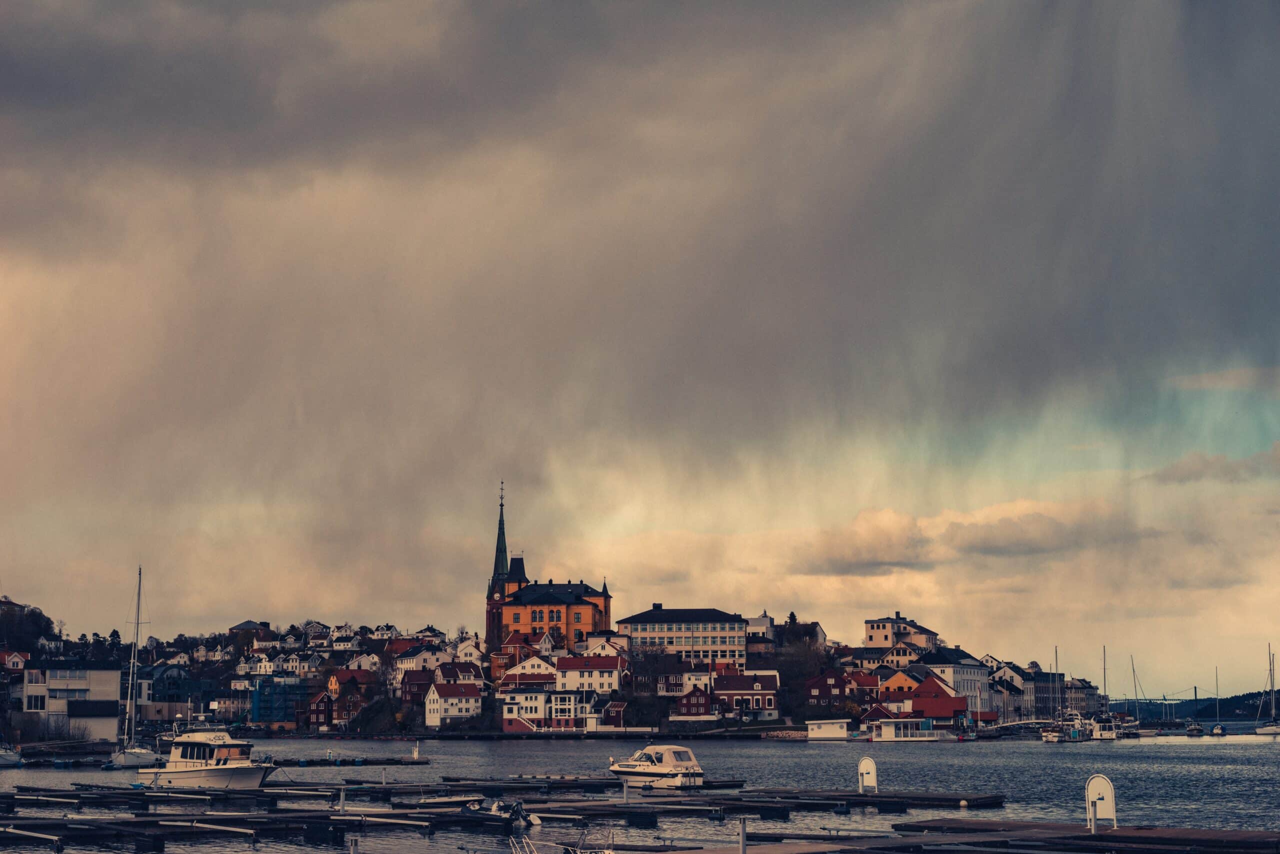 Utsikt til Arendal sentrum fra en brygge. Båter og vann, trehus og kirke.