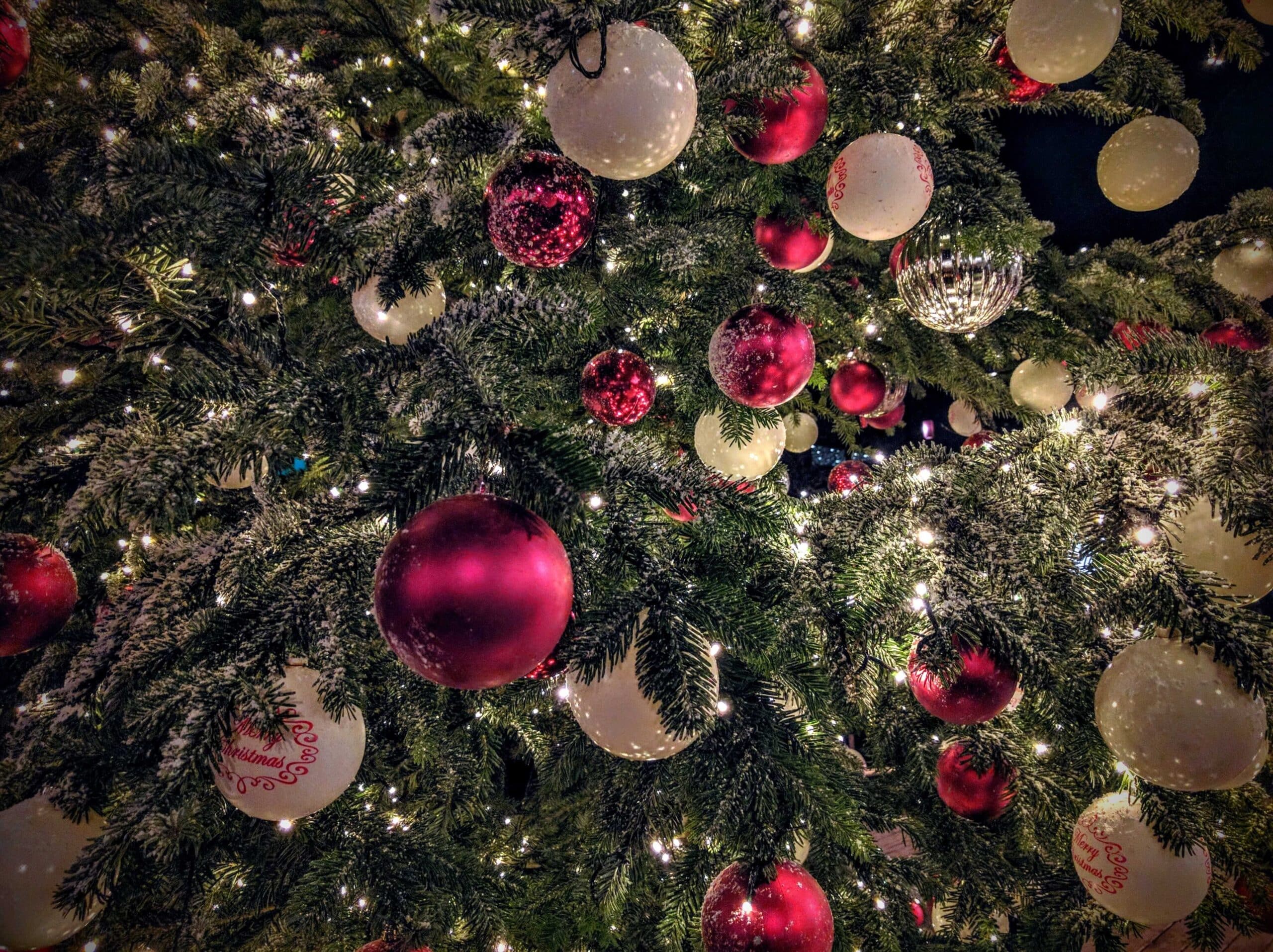 Julepynt i rødt, gull og hvitt henger på grenene av et rikt dekorert juletre med små lys.