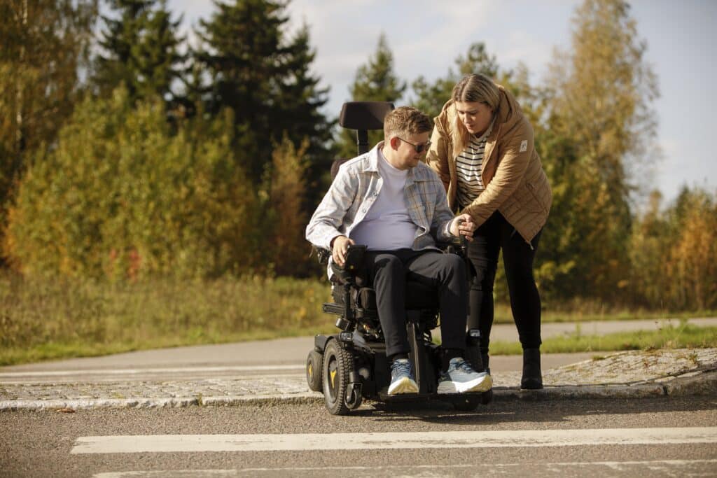Bilde av en mann i rullestol og en kvinne som står ved siden av. Kan illustrere rehabilitering.