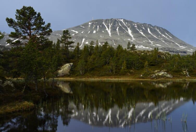 Fjellet Gaustadtoppen speilet i en rolig innsjø omgitt av skog.