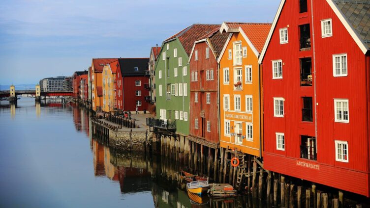 Fargerike trehus ved vannet i Trondheim, reflektert i vannoverflaten. Høstlig lys gir en varm atmosfære til den ikoniske bryggerekken.