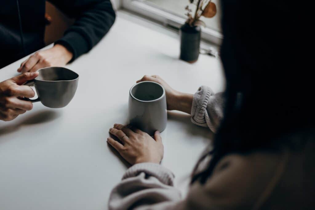 Illustrasjonsbilde som viser to personer som sitter ved et bord med en kaffekopp. Begge har hendene på bordet. Kan brukes for å illustrere kurs for likepersoner.